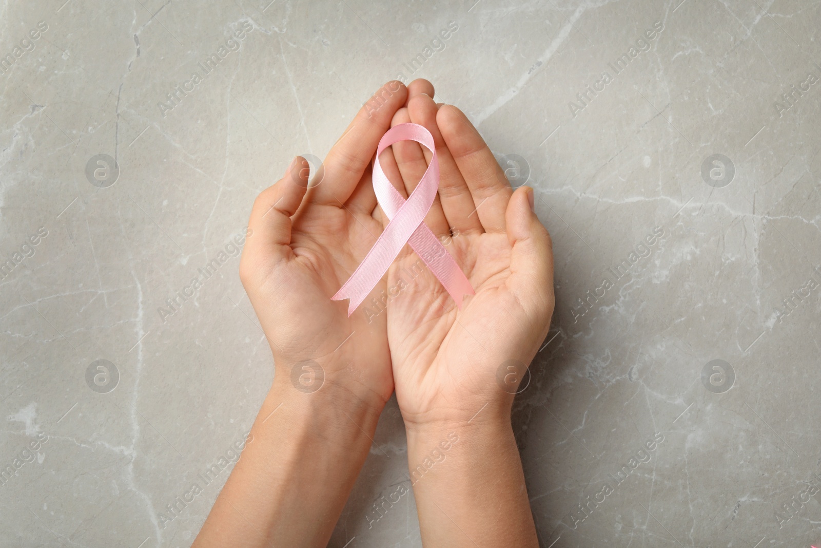 Photo of Woman holding pink ribbon on grey background, top view. Breast cancer awareness concept