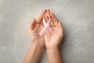 Woman holding pink ribbon on grey background, top view. Breast cancer awareness concept