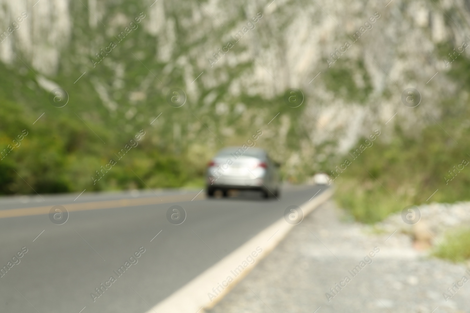 Photo of Big mountains and trees near road with white car, blurred view