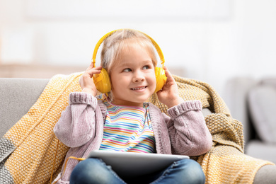 Photo of Cute little girl with headphones and tablet on sofa at home