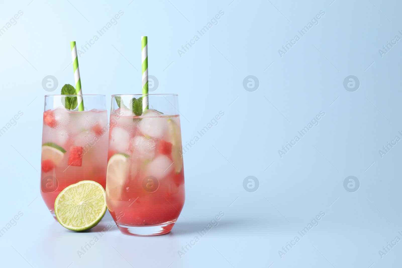 Photo of Tasty summer watermelon drink with lime in glasses on pale light blue background. Space for text