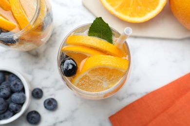 Flat lay composition of delicious orange lemonade with soda water, mint and blueberries on white marble table. Fresh summer cocktail