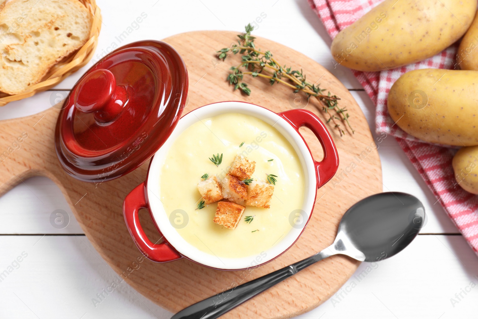 Photo of Tasty potato soup with croutons and rosemary in ceramic pot served on white wooden table, flat lay