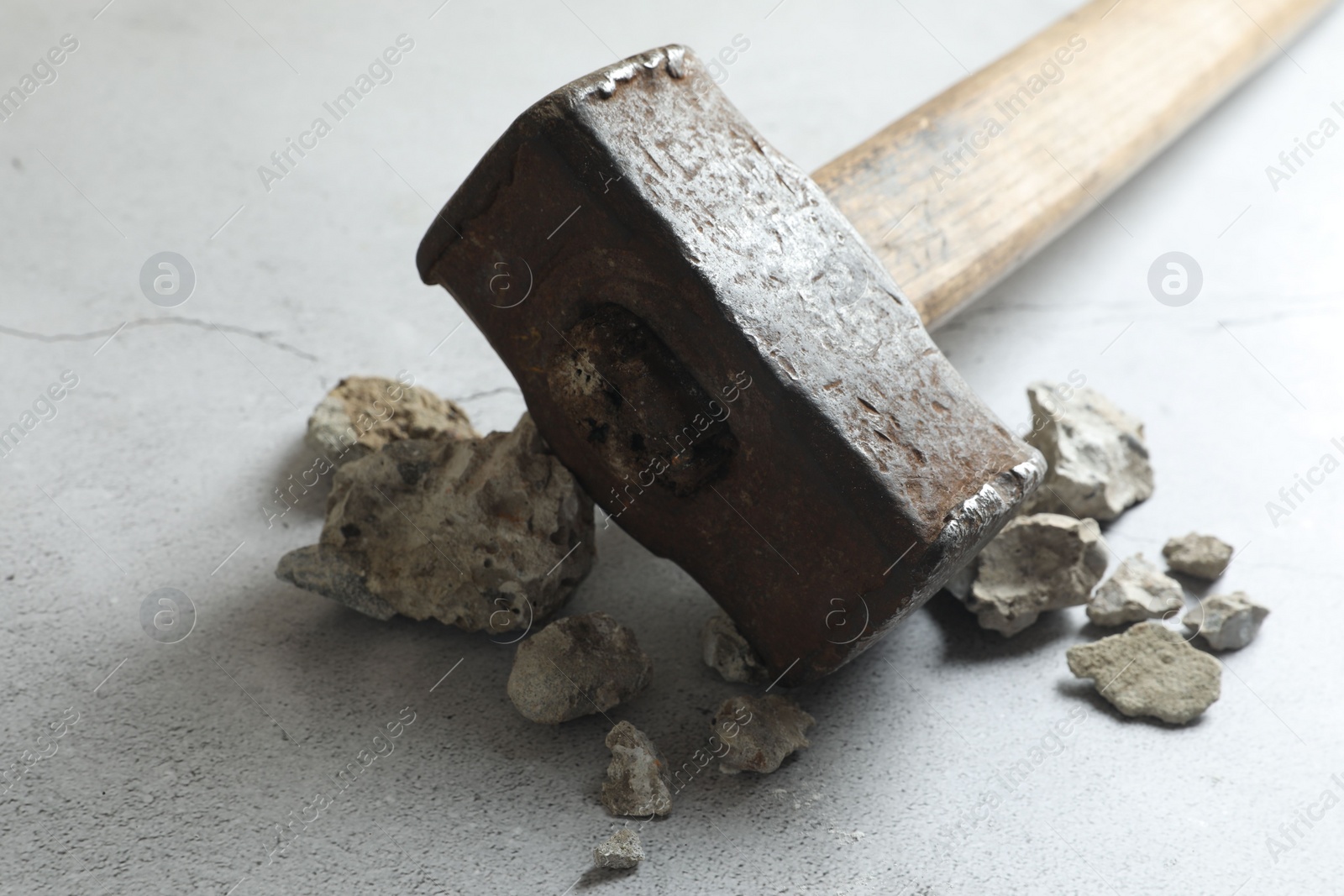 Photo of One sledgehammer and pieces of broken stones on grey textured background, closeup