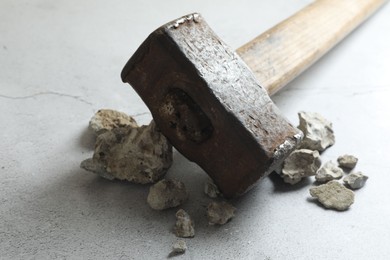 Photo of One sledgehammer and pieces of broken stones on grey textured background, closeup