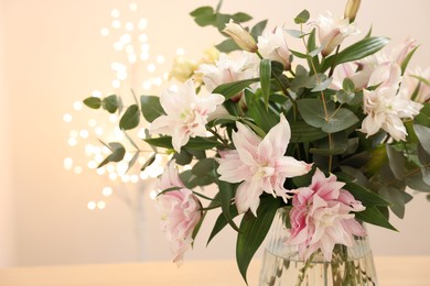 Bouquet of beautiful lily flowers in vase against beige background with blurred lights, closeup