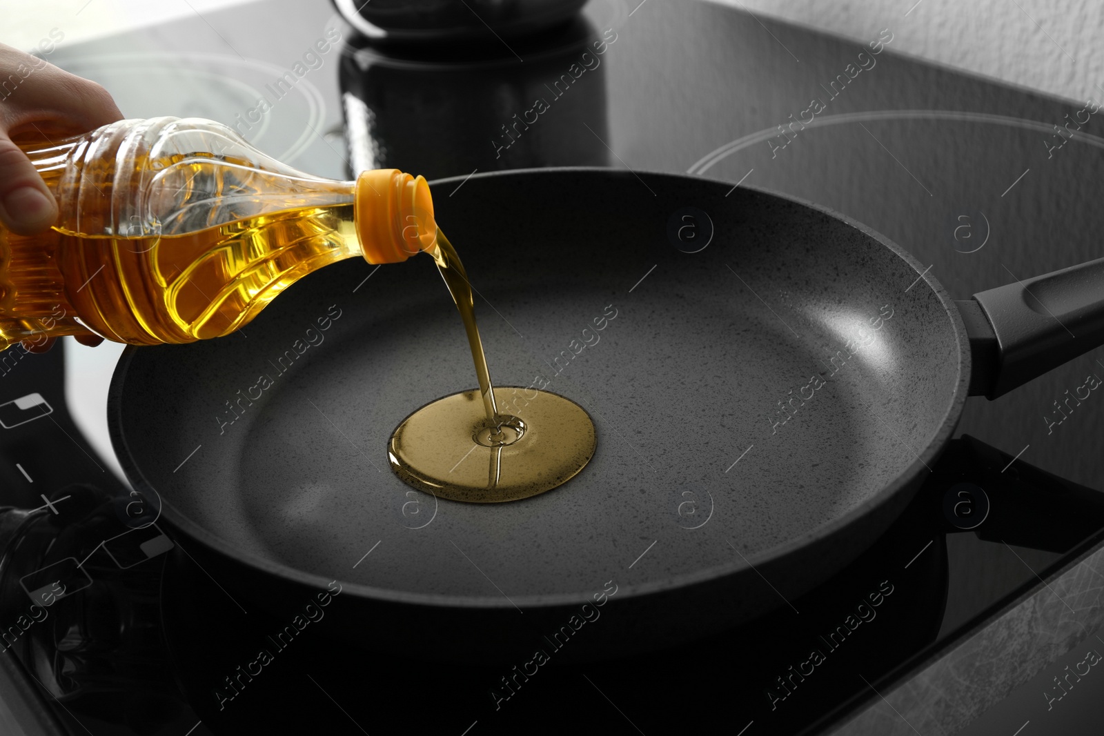 Photo of Woman pouring cooking oil from bottle into frying pan, closeup