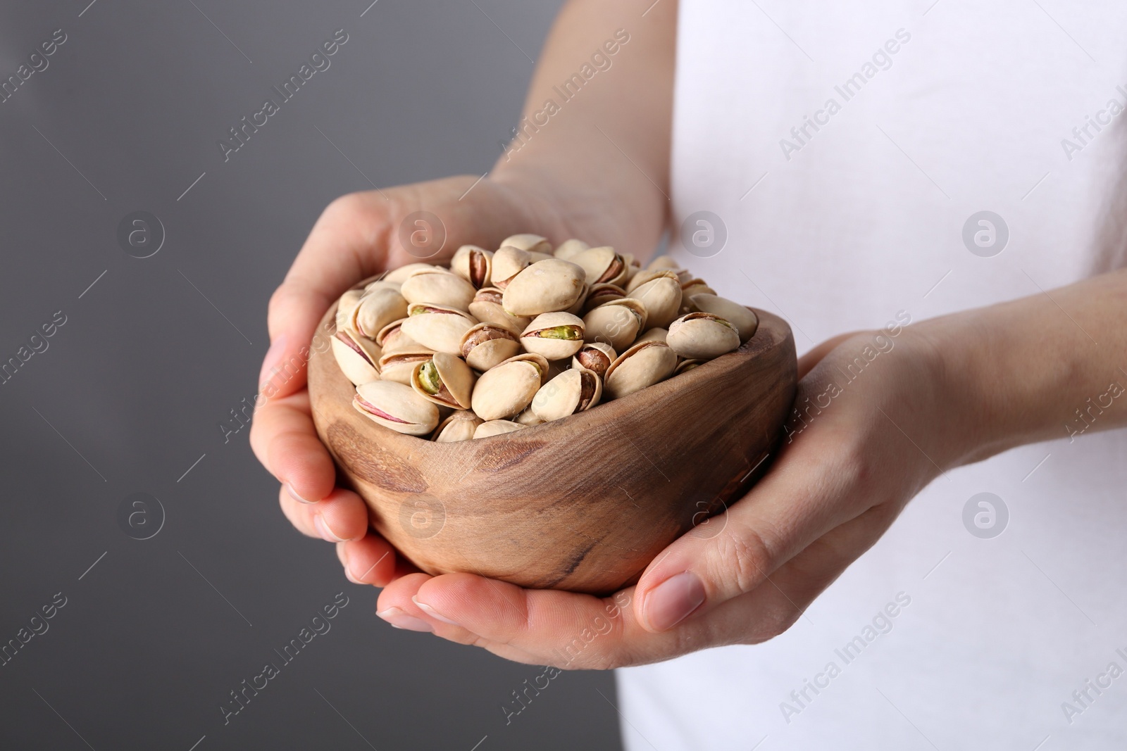 Photo of Woman holding tasty pistachios in bowl on grey background, closeup