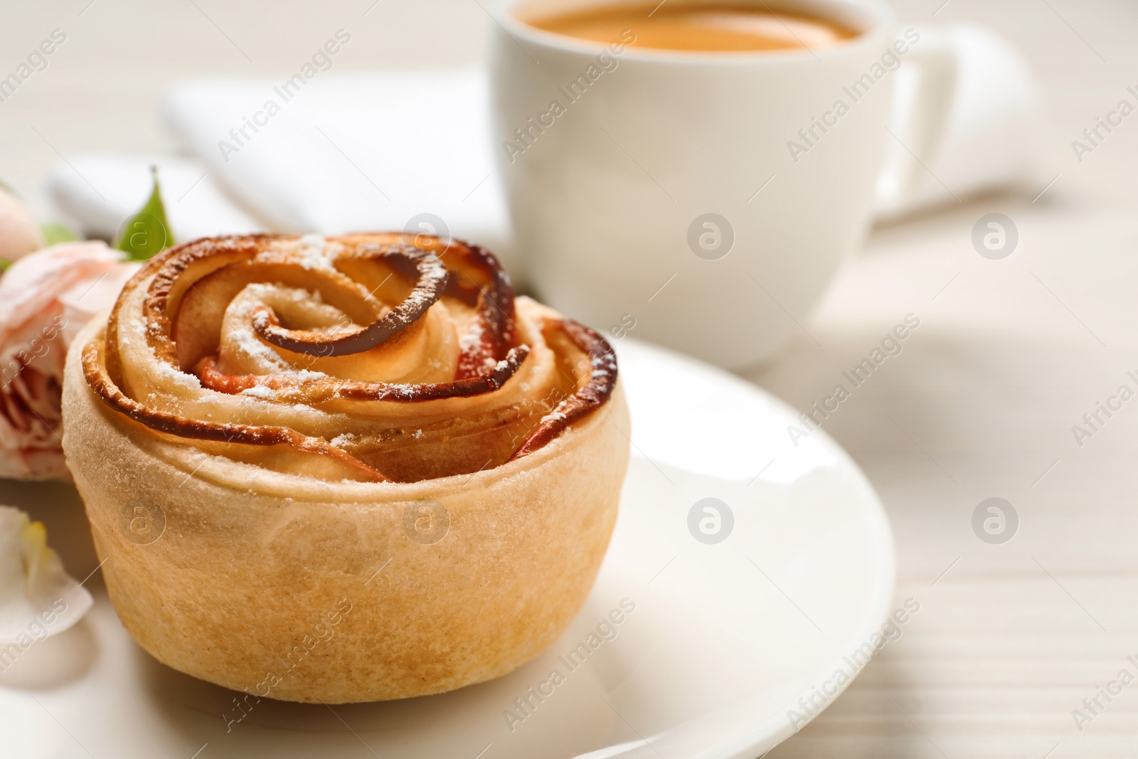 Photo of Freshly baked apple rose, cup of coffee and beautiful flowers on white wooden table