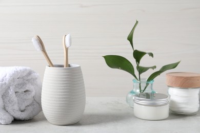Photo of Bamboo toothbrushes in holder, towel, cotton pads and leaves on light grey table