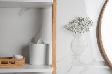 Photo of Silicone vase with flowers on white marble wall and shelving unit in stylish bathroom