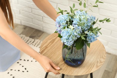 Photo of Woman adjusting table with beautiful blue hortensia flowers indoors