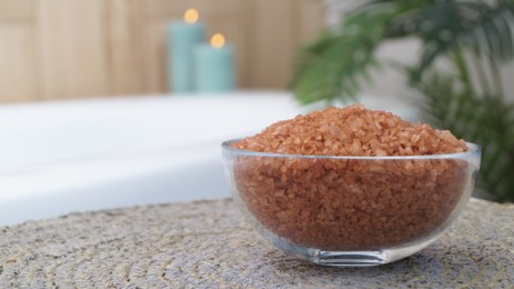 Photo of Glass bowl of bath salt on wicker mat in bathroom, closeup. Space for text
