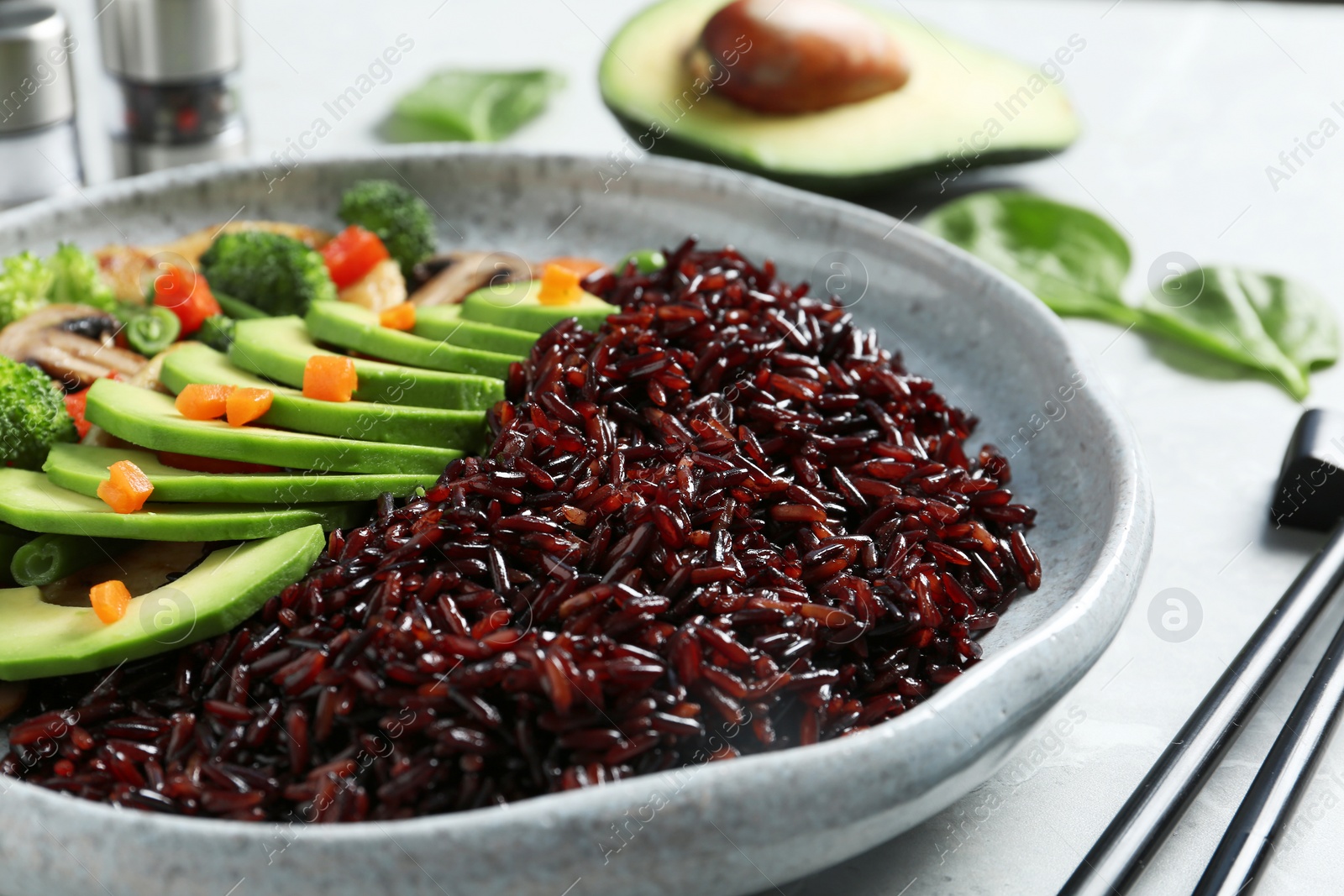 Photo of Plate of boiled brown rice with avocado on table, closeup