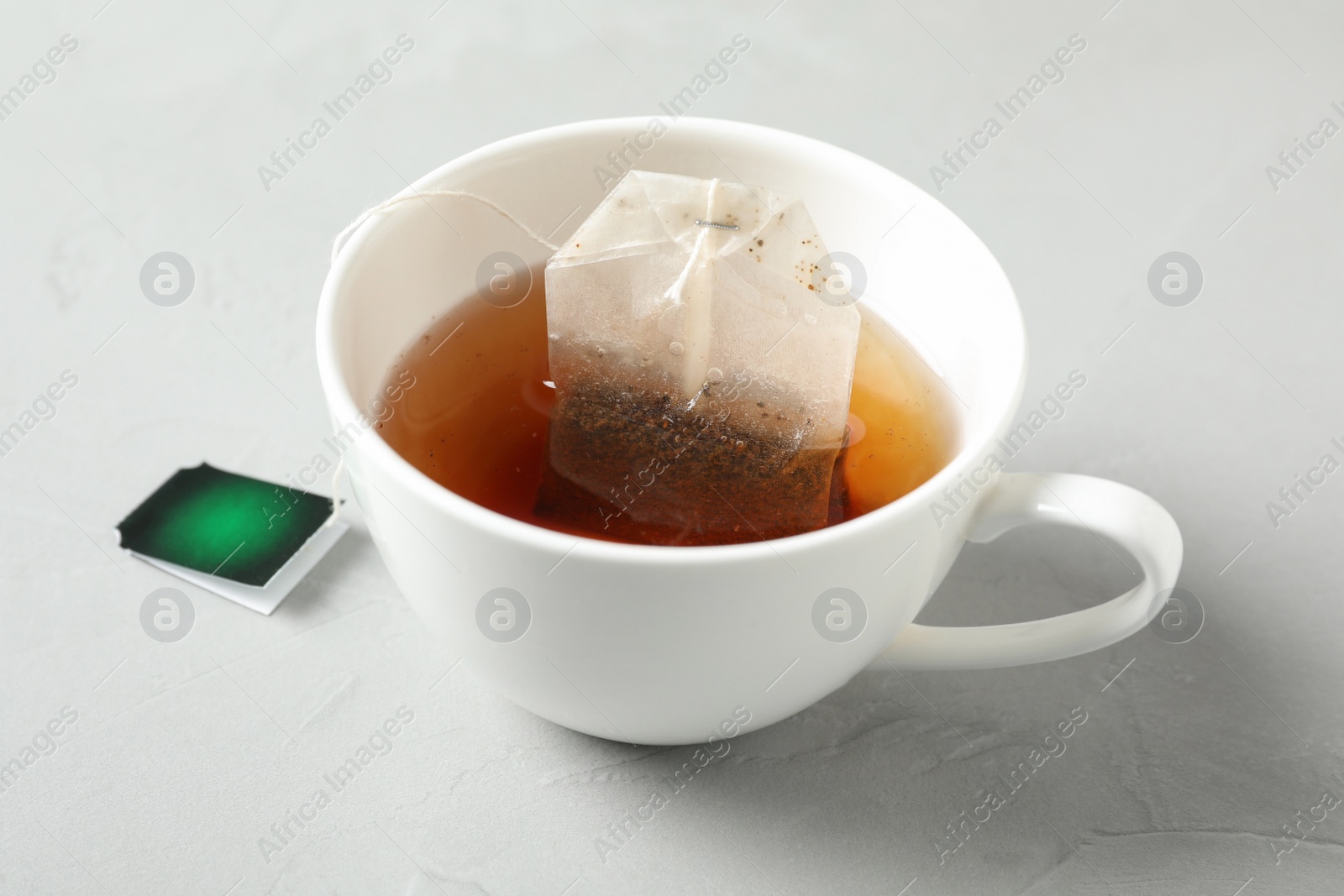 Photo of Tea bag in cup of hot water on light grey table