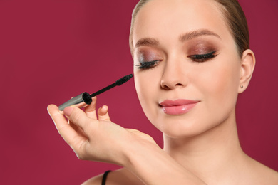Photo of Artist applying makeup onto woman's face on pink background, closeup