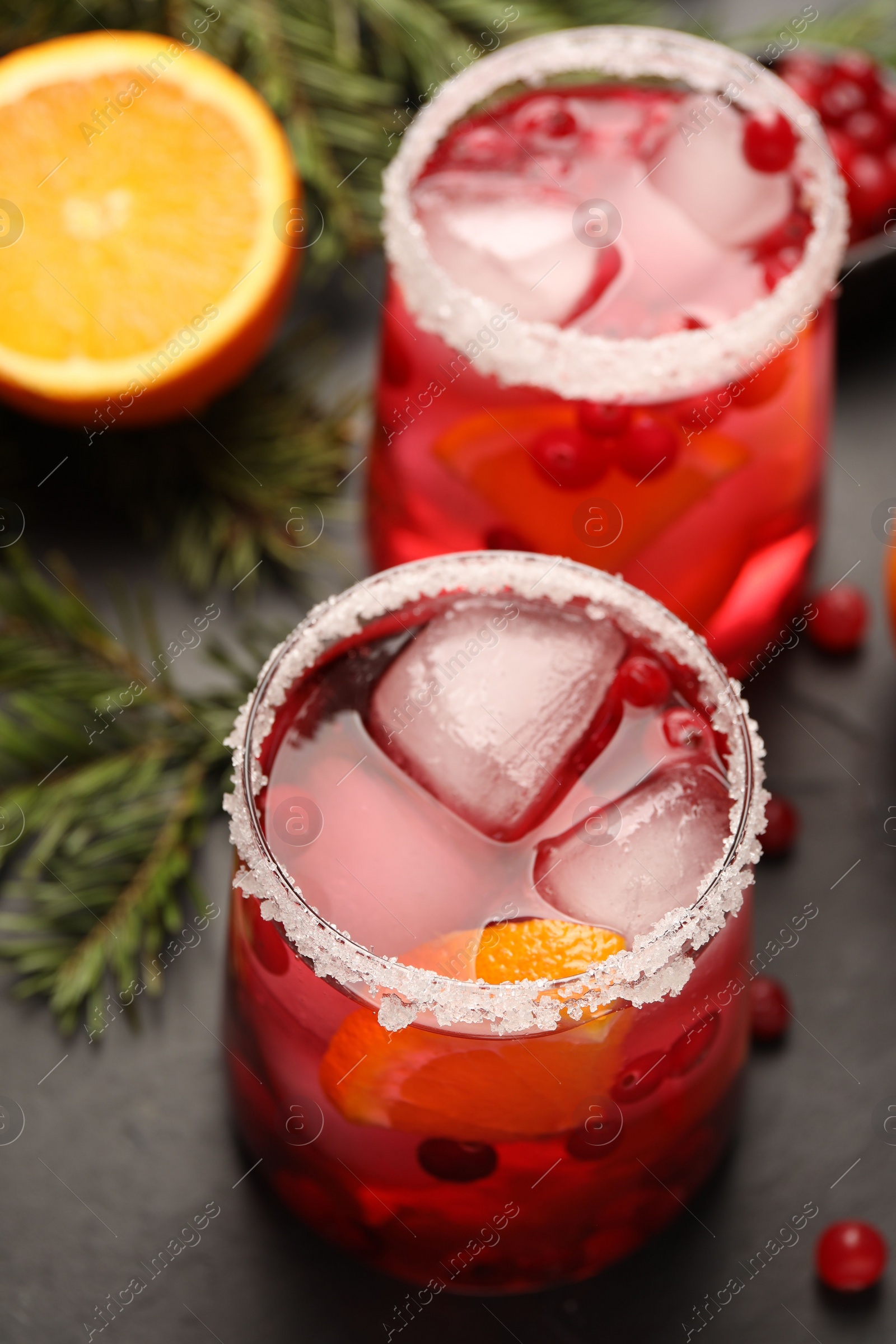 Photo of Tasty cranberry cocktail with ice cubes in glasses on dark gray table, closeup