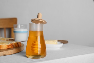 Photo of Jar of tasty honey, milk and bread with butter on white table. Space for text