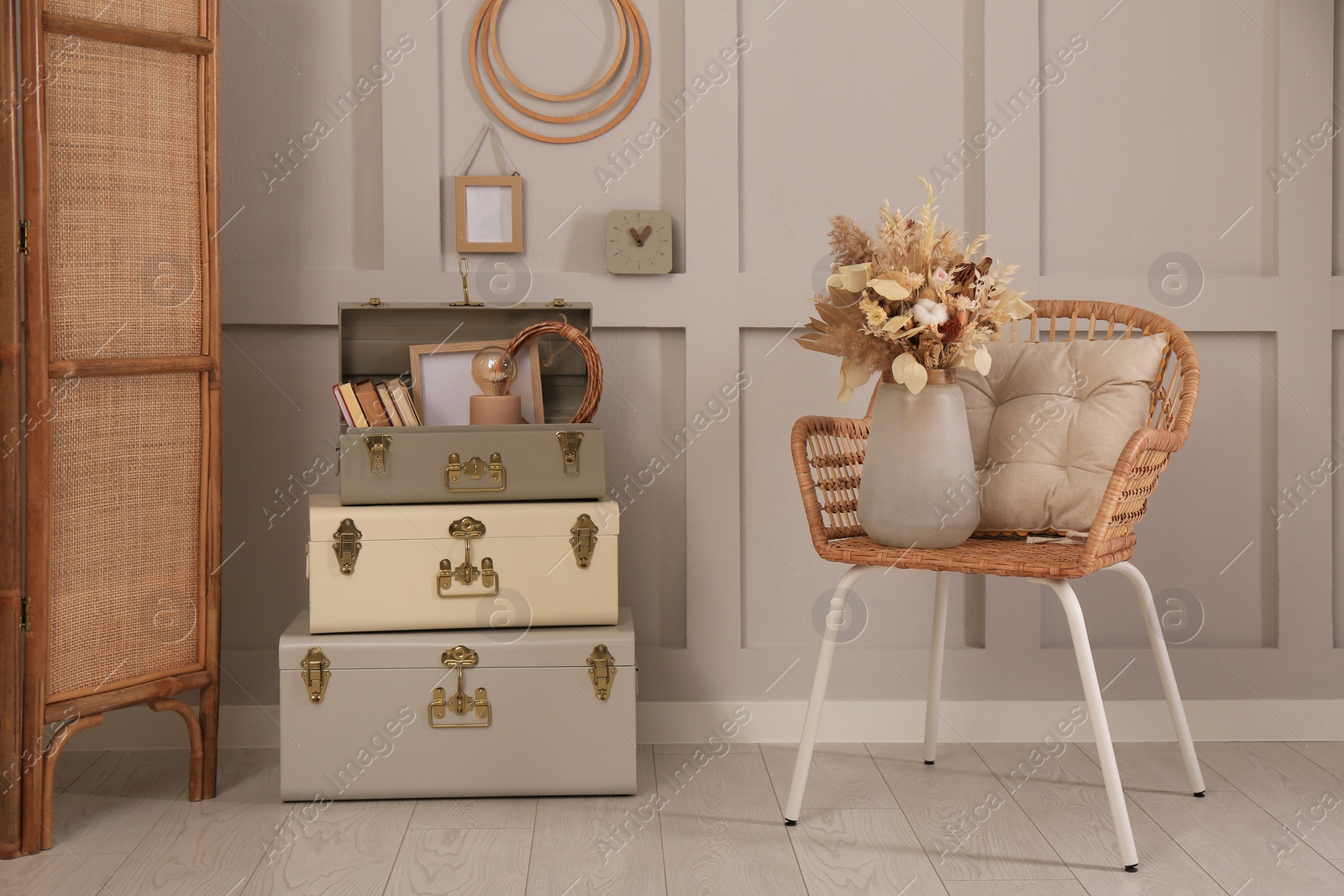 Photo of Wicker chair with dry flowers and storage trunks indoors. Interior design