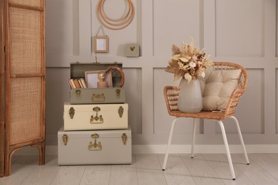 Wicker chair with dry flowers and storage trunks indoors. Interior design
