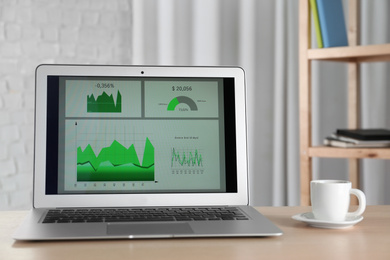 Photo of Modern laptop and cup of coffee on desk in office