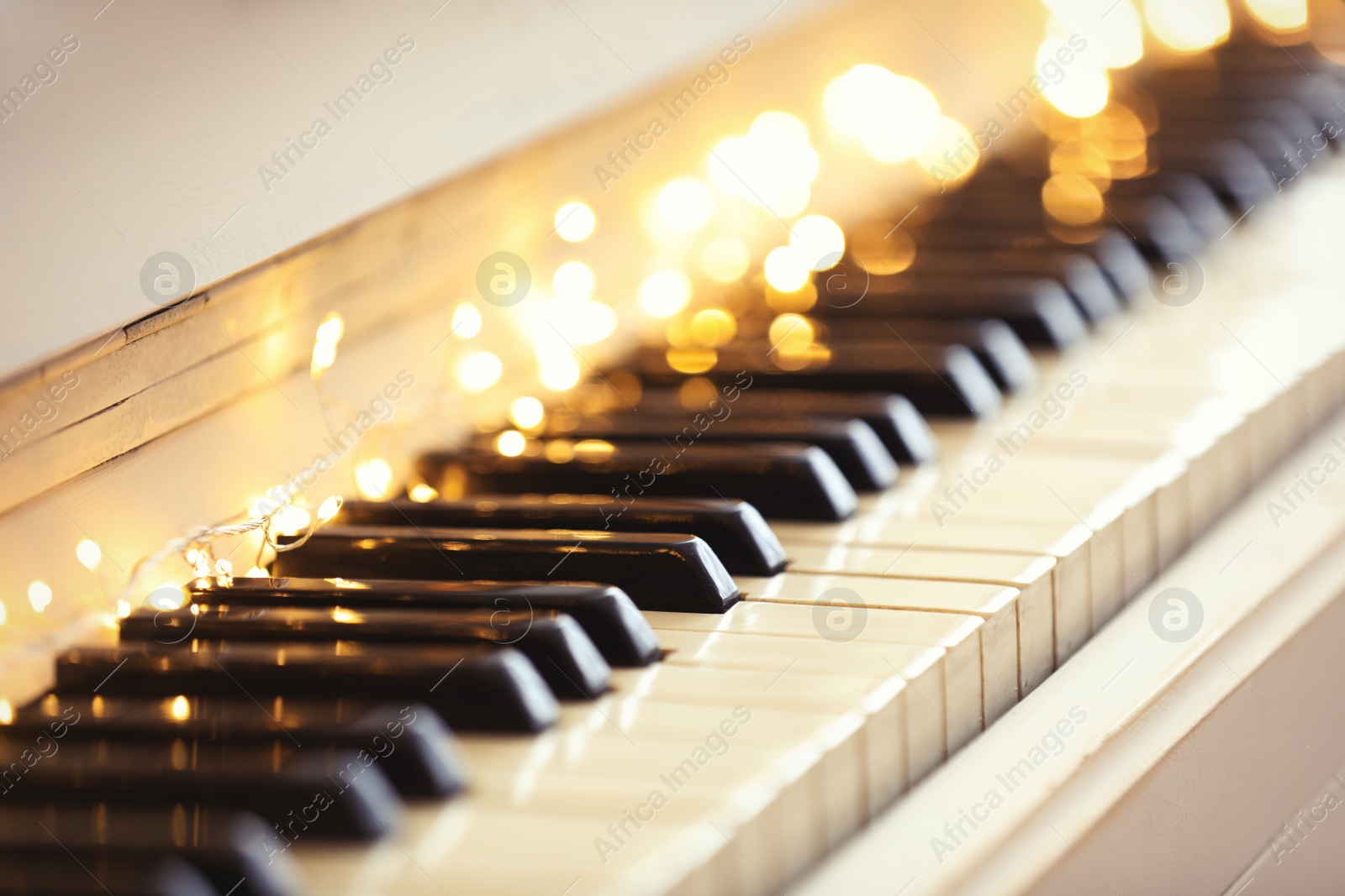 Photo of Glowing fairy lights on piano keys, closeup. Christmas music