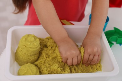 Photo of Little girl playing with bright kinetic sand at table, closeup