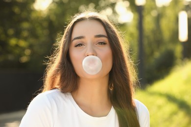 Photo of Beautiful young woman blowing bubble gum in park