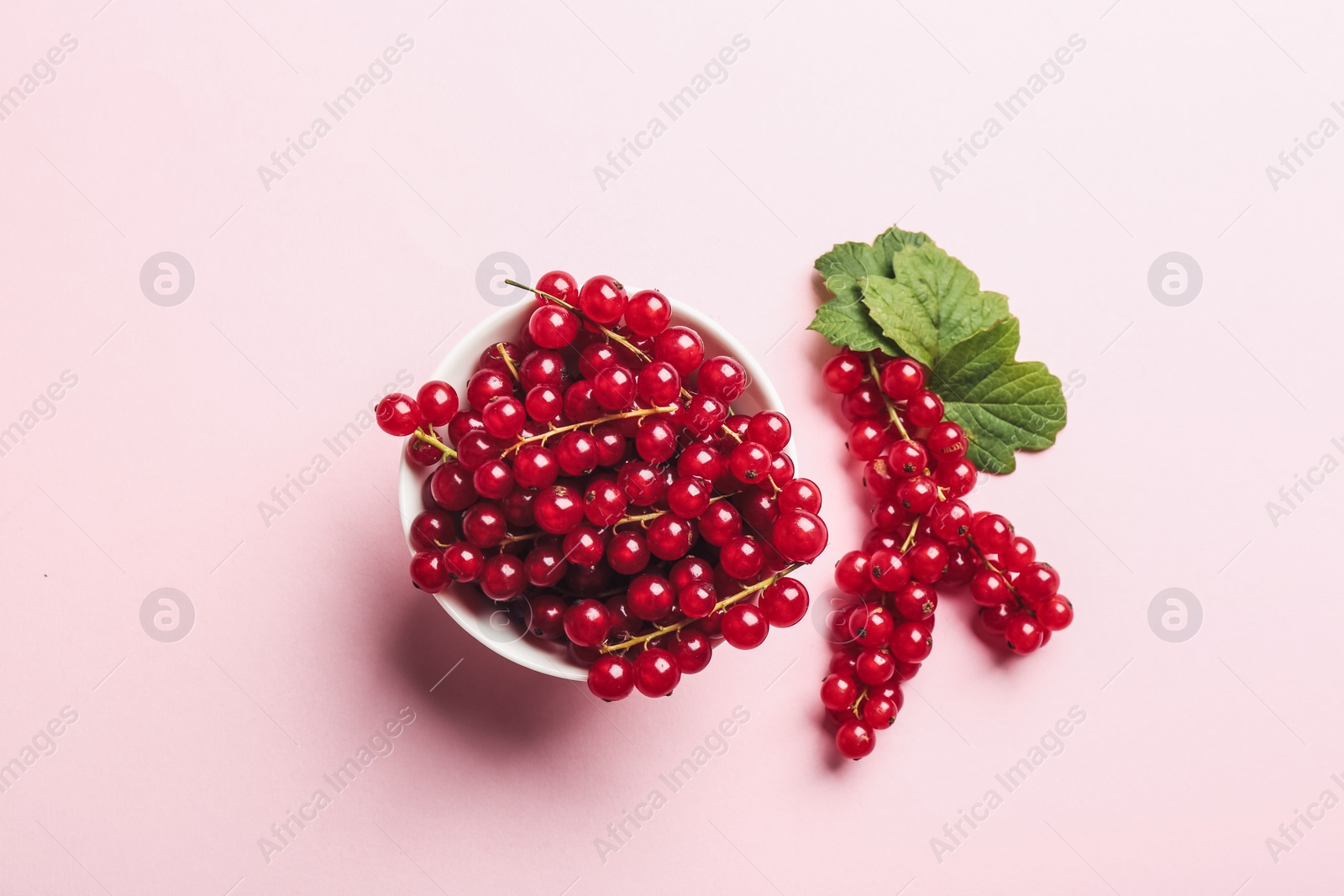 Photo of Delicious red currants and leaves on pink background, flat lay