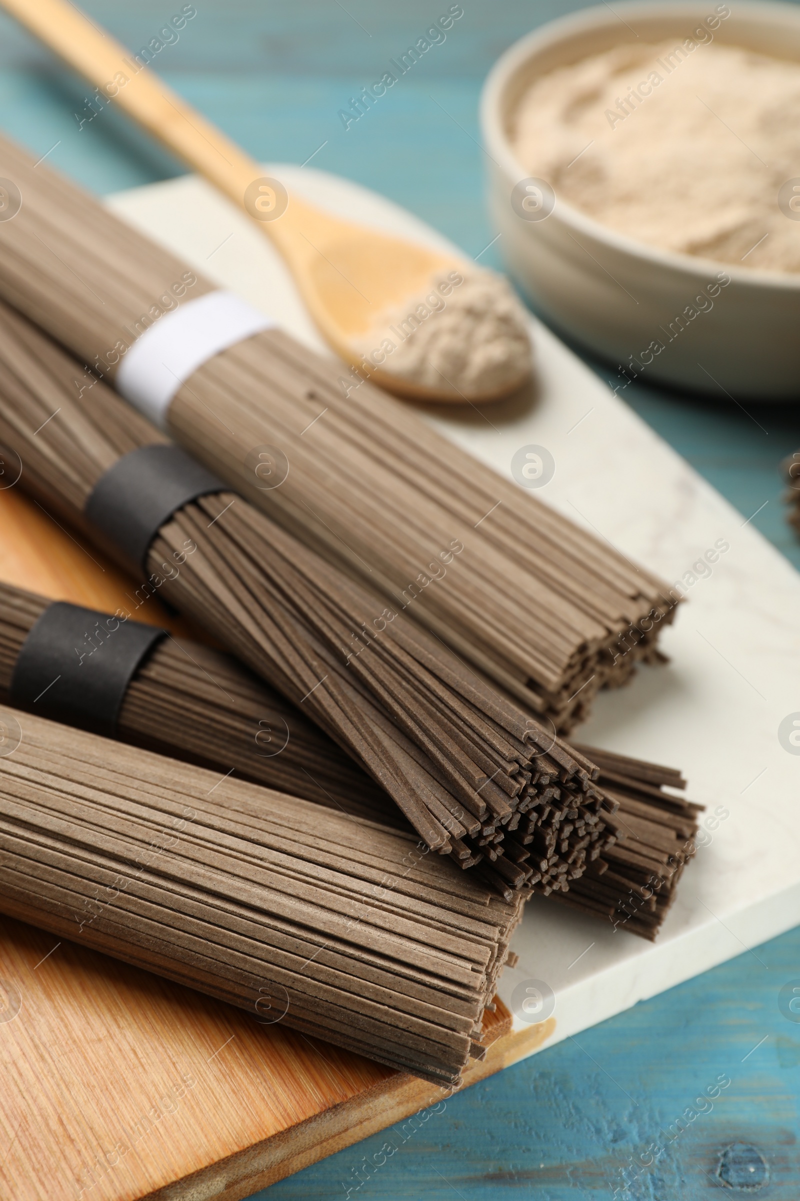 Photo of Uncooked buckwheat noodles (soba) on light blue wooden table, closeup