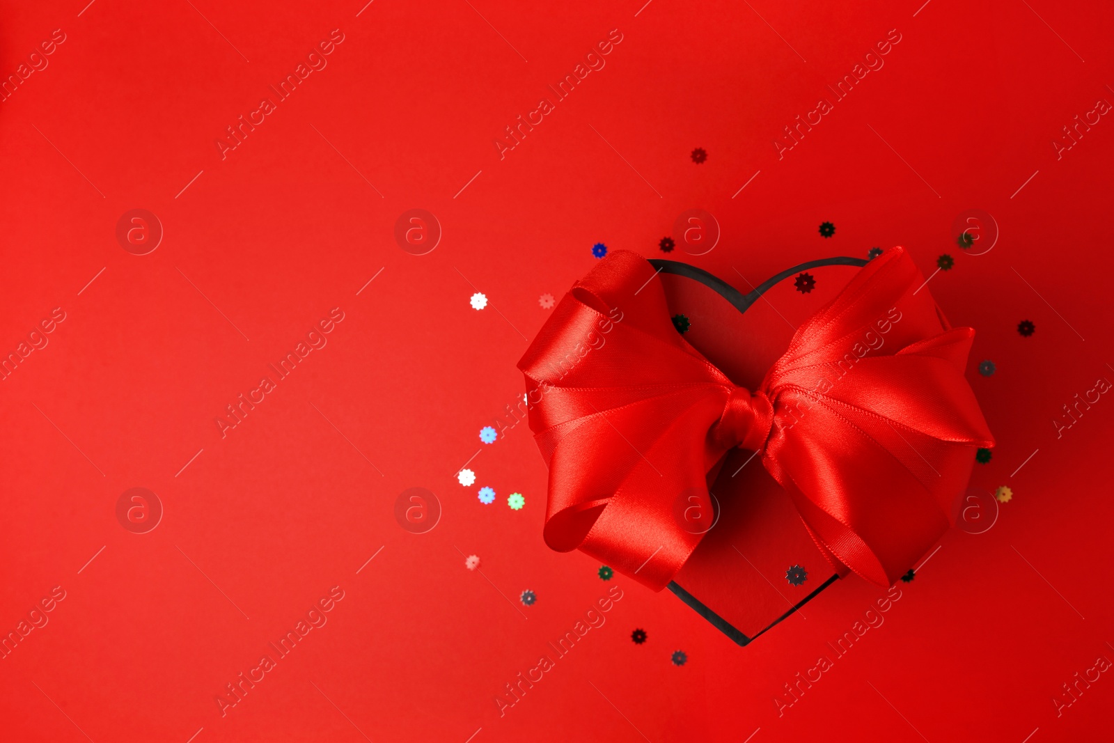 Photo of Beautiful heart shaped gift box with bow and confetti on red background, top view. Space for text