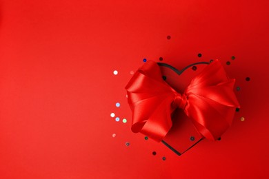 Photo of Beautiful heart shaped gift box with bow and confetti on red background, top view. Space for text
