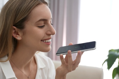 Photo of Young woman using voice search on smartphone indoors, closeup