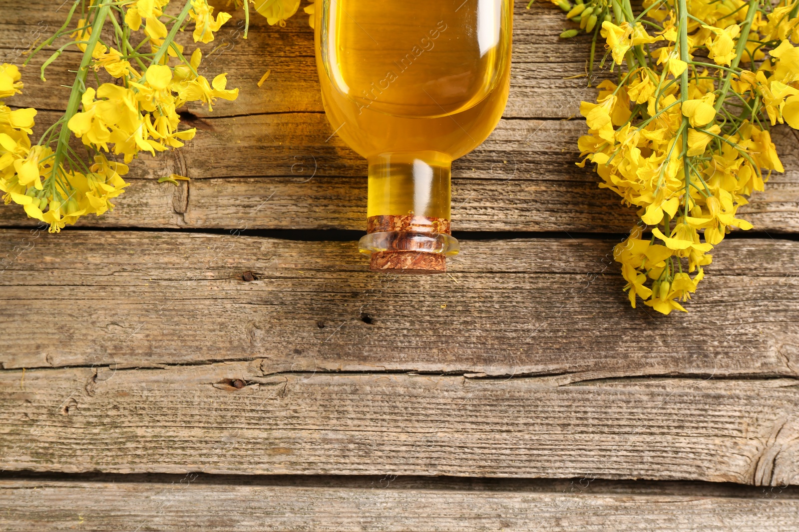 Photo of Rapeseed oil in glass bottle and beautiful yellow flowers on wooden table, flat lay. Space for text