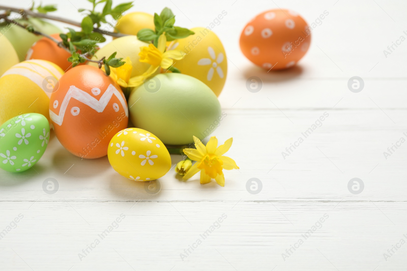 Photo of Colorful Easter eggs and flowers on white wooden table