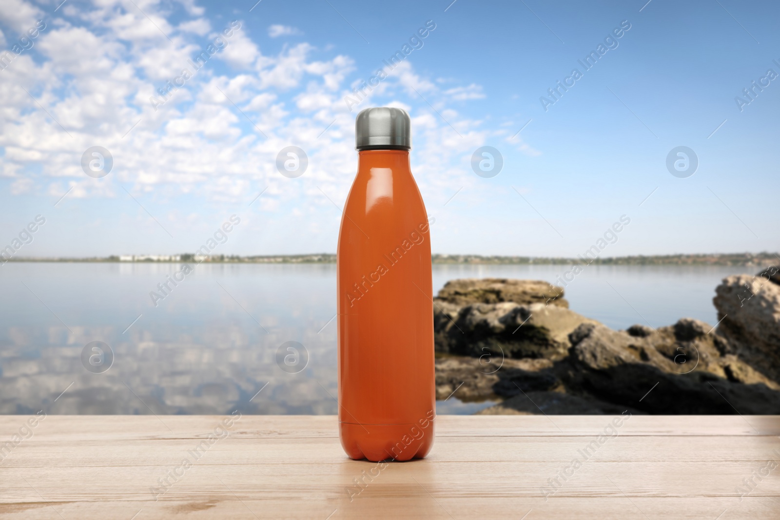 Image of Thermo bottle on wooden table near sea under blue sky