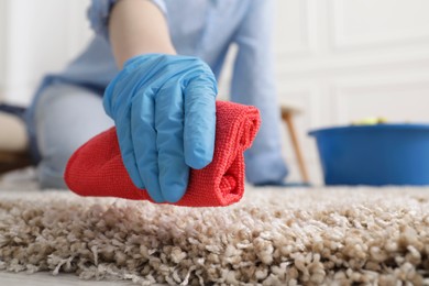 Woman in rubber gloves cleaning carpet with rag indoors, closeup. Space for text