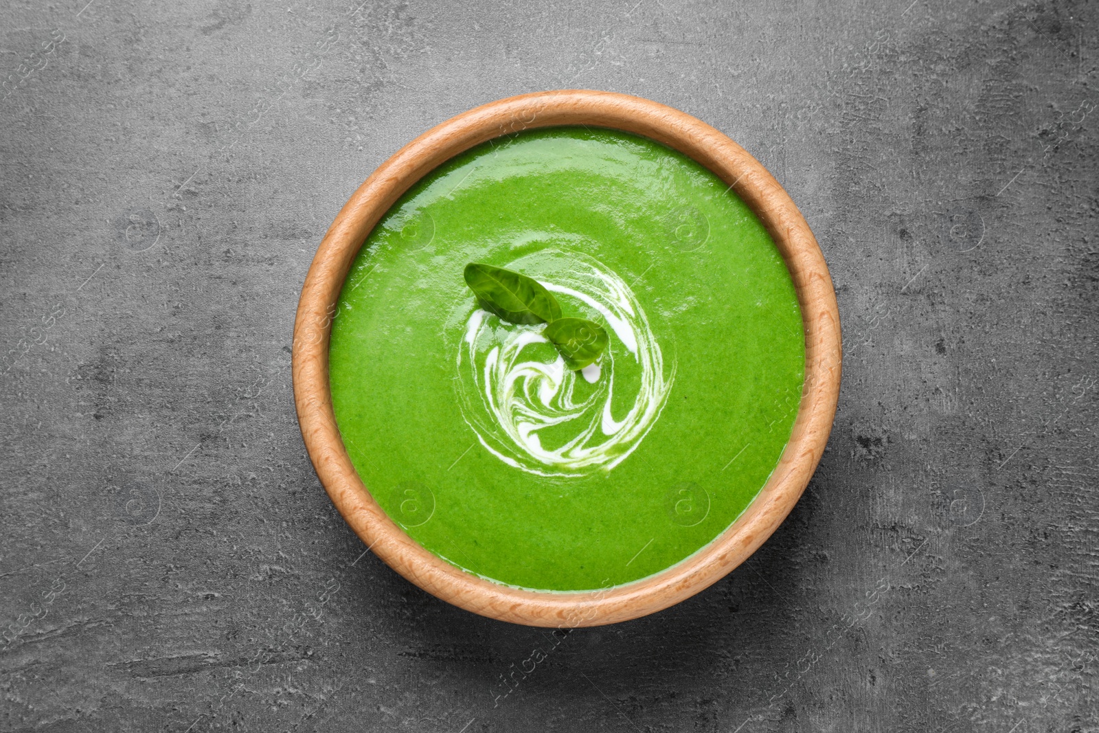 Photo of Bowl of healthy green soup with fresh spinach on grey table, top view