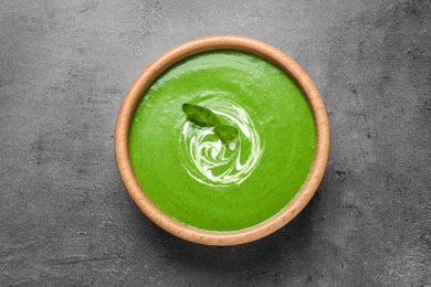 Photo of Bowl of healthy green soup with fresh spinach on grey table, top view