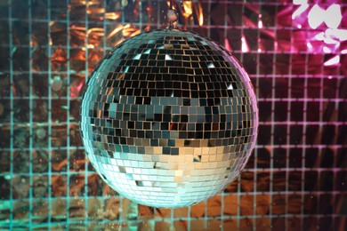 Photo of Shiny disco ball against foil party curtain under pink and turquoise light