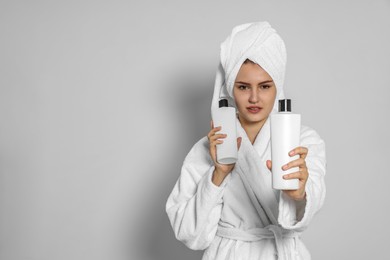 Photo of Beautiful young woman in bathrobe holding bottlesshampoo on light grey background. Space for text