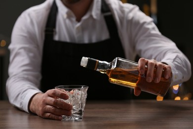 Photo of Bartender pouring whiskey from bottle into glass at bar counter indoors, closeup