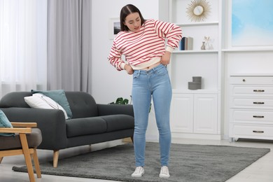 Woman trying to put on tight jeans at home