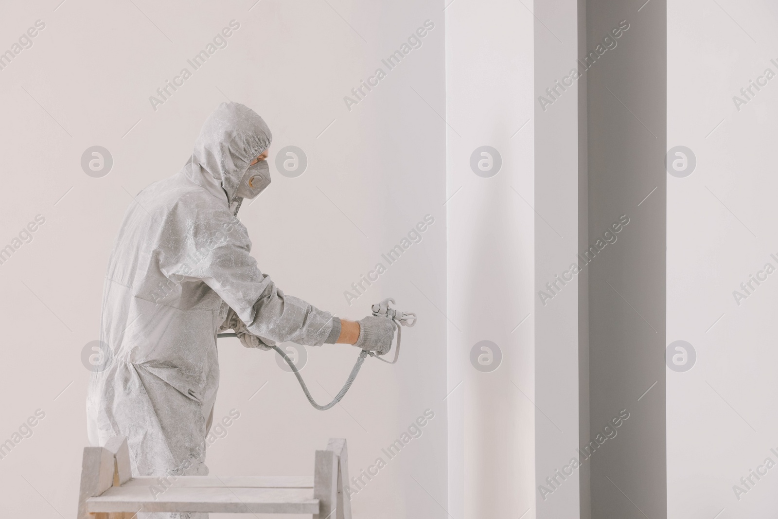 Photo of Decorator in uniform painting wall with sprayer indoors