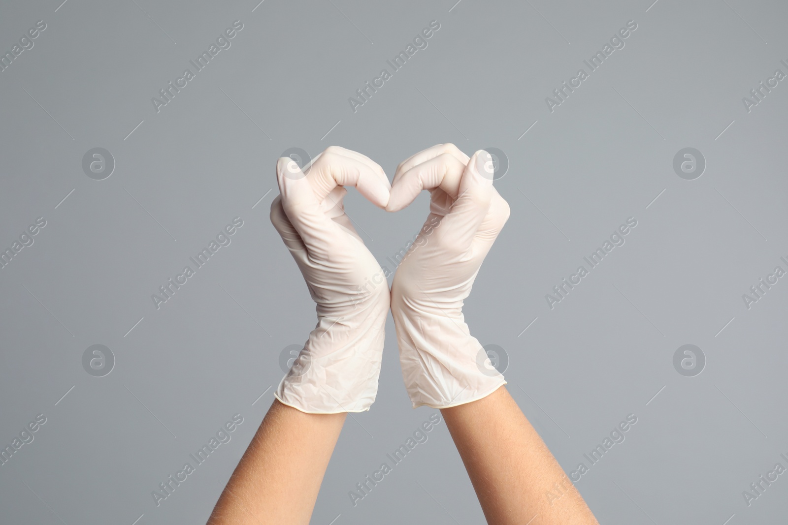 Photo of Doctor in medical gloves showing heart with hands on grey background, closeup