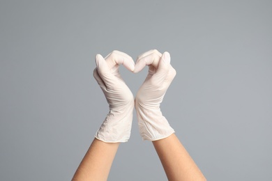 Doctor in medical gloves showing heart with hands on grey background, closeup