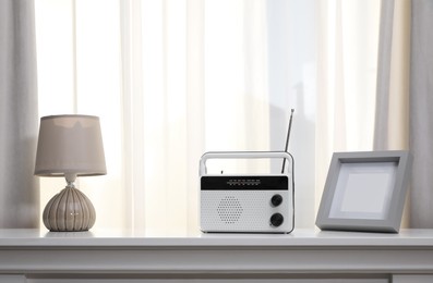 Photo of Stylish radio receiver, lamp and frame on white table near window indoors