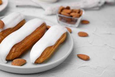 Photo of Delicious eclairs covered with glaze and almonds on white textured table, closeup. Space for text