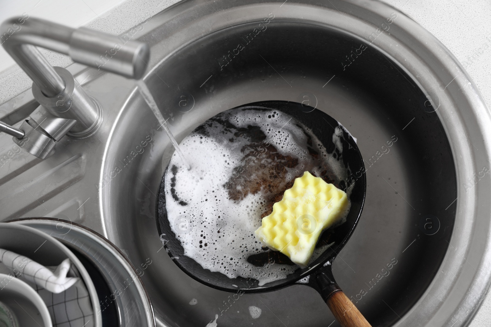 Photo of Dirty frying pan with sponge in kitchen sink, above view