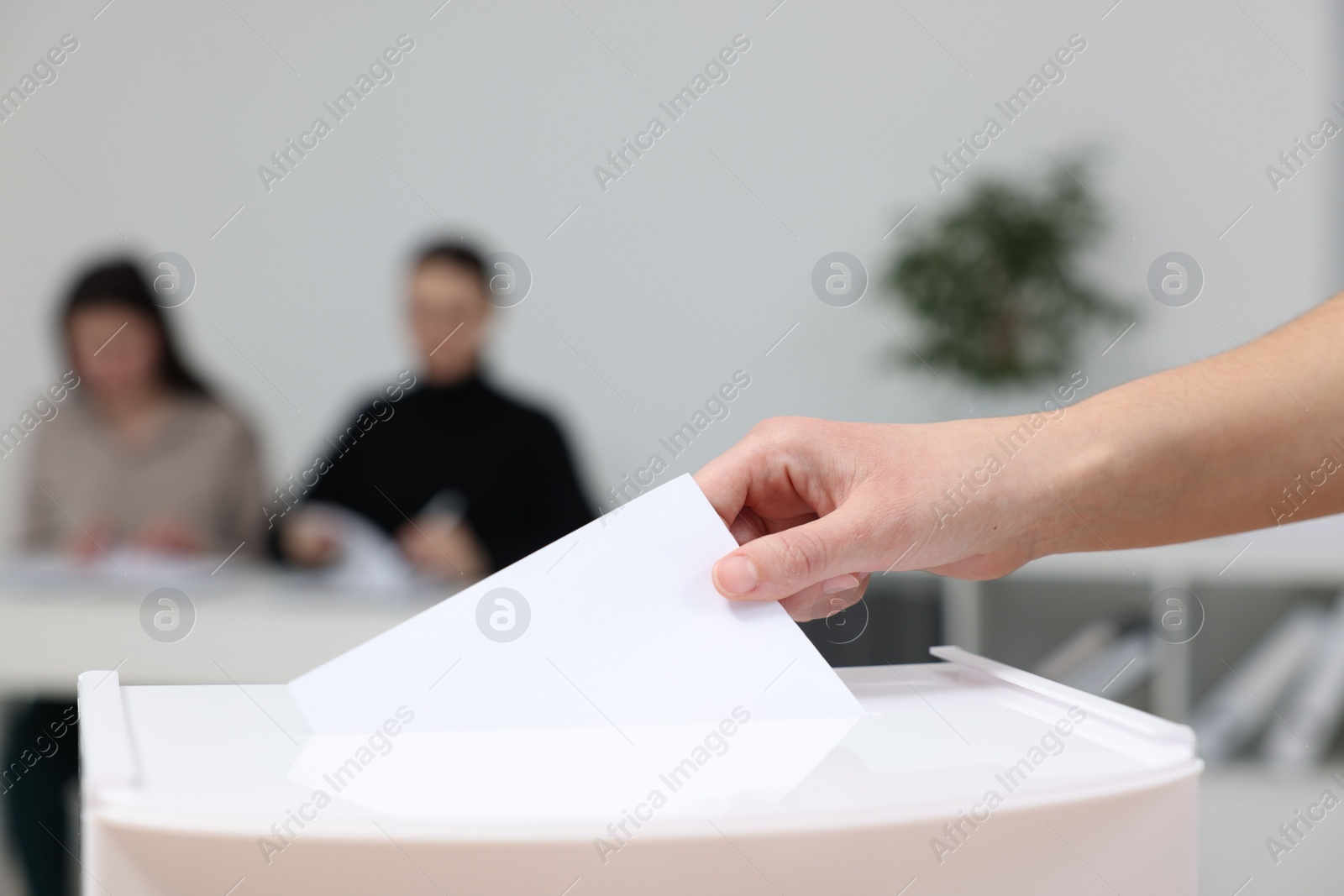 Photo of Woman putting her vote into ballot box on blurred background, closeup